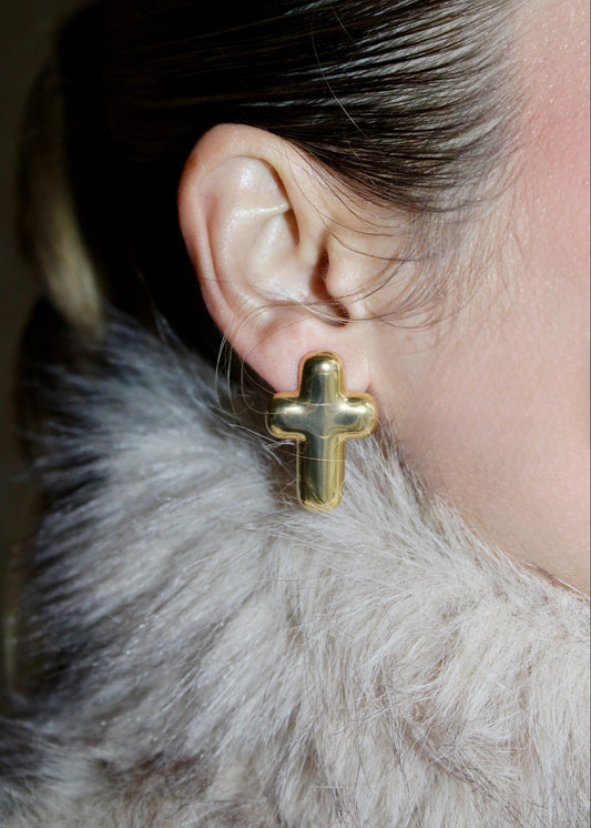 Close-up of a person wearing a gold cross earring with a fur collar.
