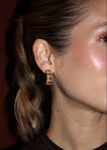 Close-up of a person wearing gold hoop earrings with a blurred background